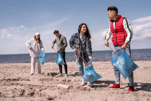 Cheerful group of volunteers with trash bags picking up rubbish with grabber tools — Stock Photo