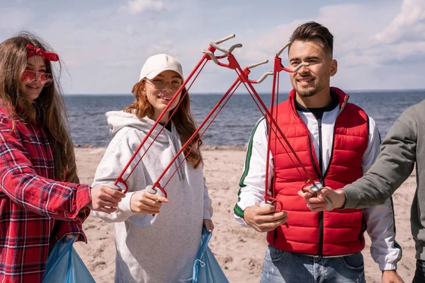 Luz del sol en voluntarios felices sosteniendo herramientas de recogida juntos - foto de stock