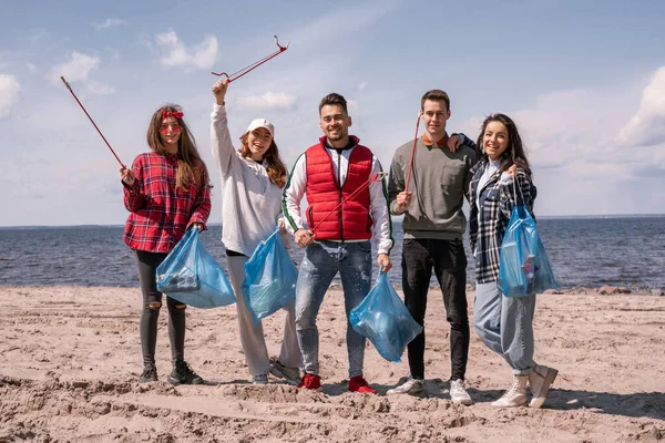 Grupo de voluntarios felices sosteniendo recoger herramientas y bolsas de basura - foto de stock