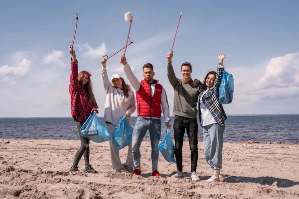 Grupo de voluntarios alegres sosteniendo recoger herramientas y bolsas de basura - foto de stock