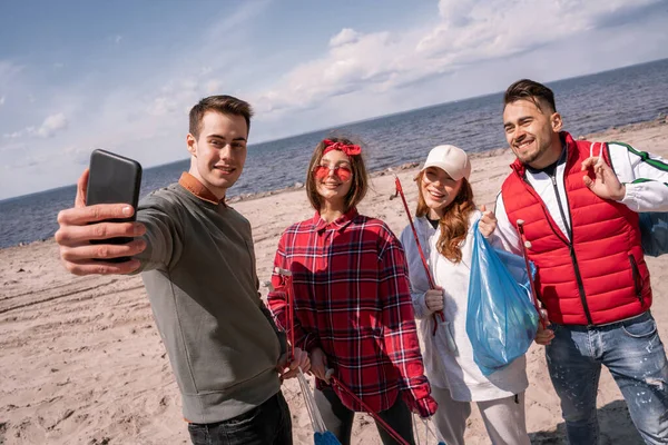 Heureux jeune homme prendre selfie avec des amis tout en ramassant des ordures — Photo de stock