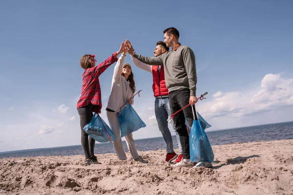 Group of cheerful volunteers holding trash bags and giving high five — Stock Photo
