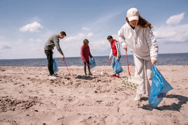 Group of volunteers holding trash bags picking up rubbish on sand — Stock Photo