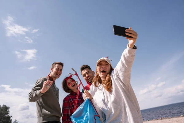 Cheerful woman taking selfie with friends while picking up trash — Stock Photo