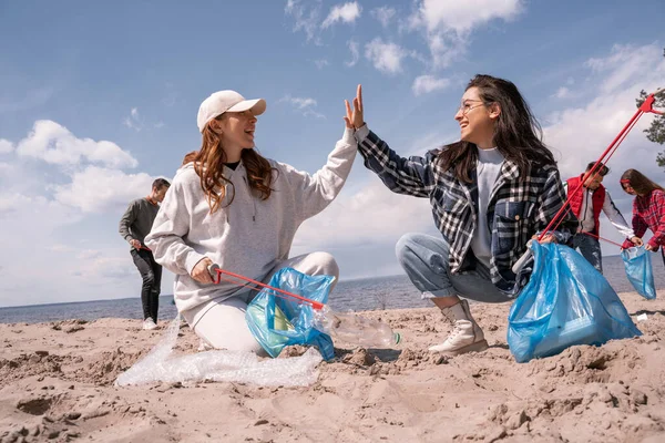 Glückliche junge Frauen mit Greifern, die High Five geben, während sie draußen Müll sammeln — Stockfoto