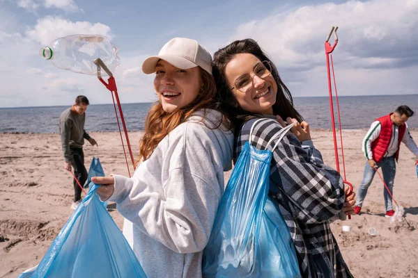 Mujeres jóvenes felices con agarradores y bolsas de basura fuera - foto de stock