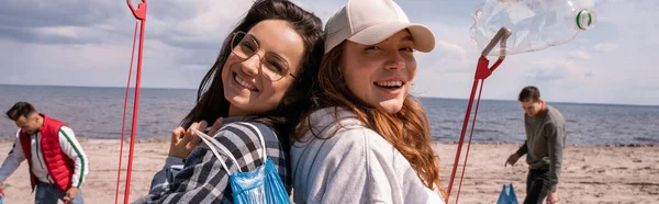 Happy young women with grabbers and trash bags outside, banner — Stock Photo