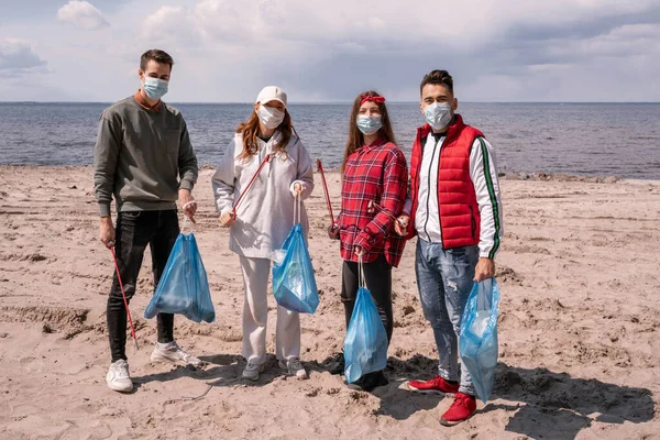 Mulheres jovens e homens em máscaras médicas segurando sacos de lixo e agarradores fora, pegar conceito de lixo — Fotografia de Stock