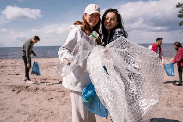 Mujeres jóvenes felices recogiendo basura plástica afuera - foto de stock
