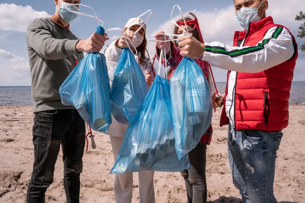 Jeunes volontaires dans des masques médicaux tenant des sacs poubelle à l'extérieur, ramasser le concept de poubelle — Photo de stock