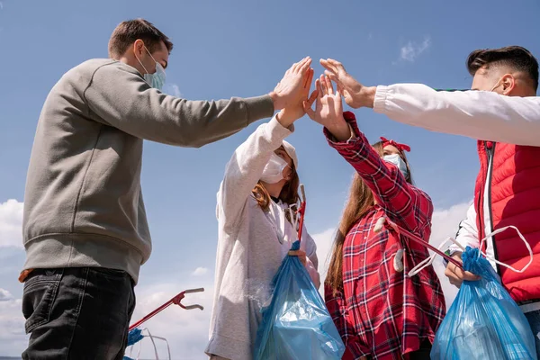 Mujeres jóvenes y hombres con máscaras médicas sosteniendo bolsas de basura y tomados de la mano, recoger el concepto de basura - foto de stock