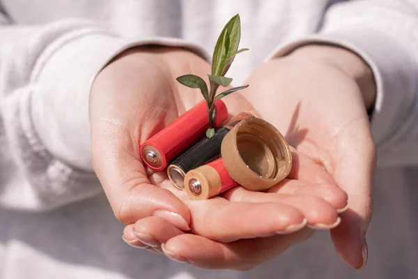 Vista ritagliata della donna che tiene le batterie, tappo di bottiglia di plastica e pianta verde in mano — Foto stock