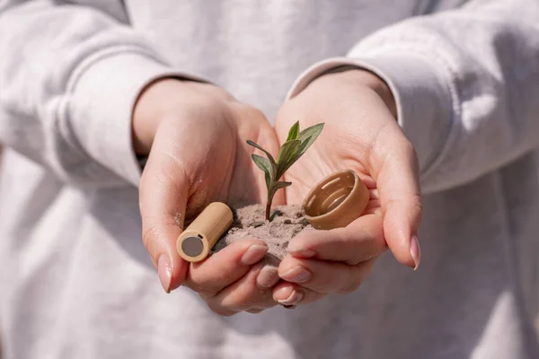 Vista recortada de la mujer sosteniendo la batería, tapa de plástico y planta verde en las manos - foto de stock