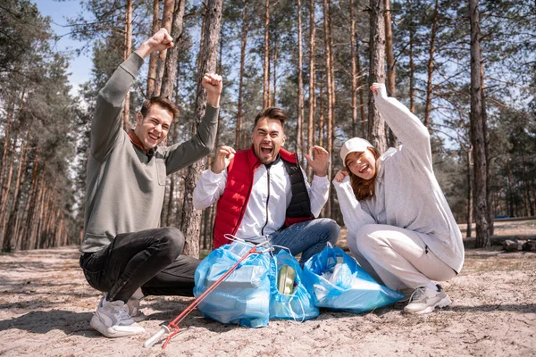 Voluntarios emocionados cerca de bolsas de basura en el bosque - foto de stock