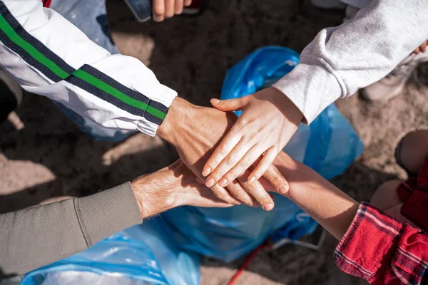 Vista superior de voluntarios tomados de la mano por encima de la bolsa de basura - foto de stock