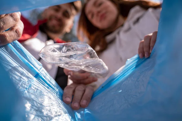 Пластикова чашка падає в мішок для сміття біля розмитих добровольців — стокове фото