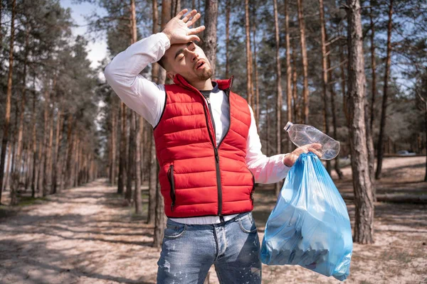 Uomo stanco che tiene sacchetto di spazzatura blu nella foresta — Foto stock