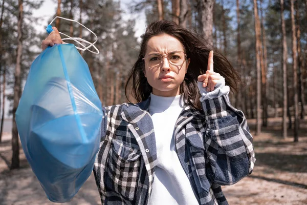 Junge Frau warnt mit Finger und hält blauen Müllsack im Wald — Stockfoto