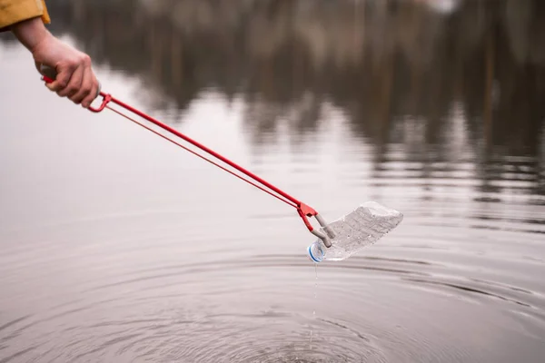 Cropped view of man holding grabber while picking up plastic bottle from lake — Stock Photo
