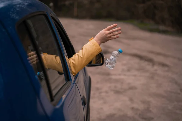 Cropped view of man throwing away empty plastic bottle from car — Stock Photo