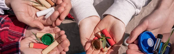 Cropped view of volunteers holding batteries, bottle caps and green plants in hands, banner — Stock Photo