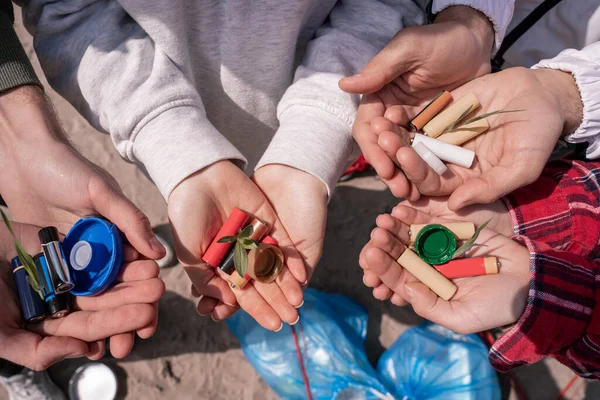 Vista cortada de voluntários segurando baterias, tampas de garrafa e plantas verdes nas mãos — Fotografia de Stock