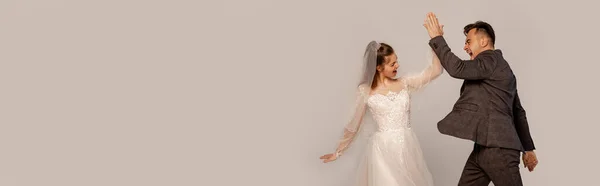 Взволнованные невеста и жених давая пять изолированных на серый, баннер — стоковое фото