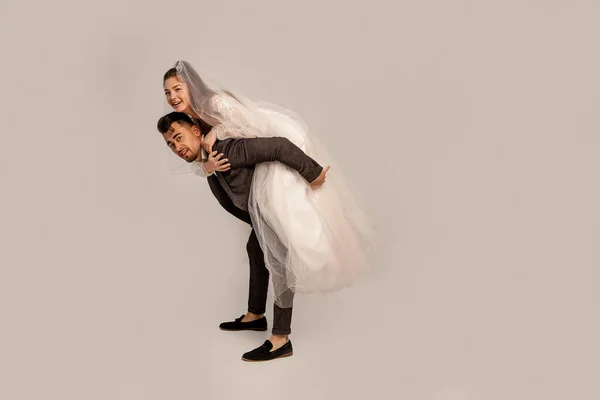 Full length view of cheerful bride piggybacking on groom isolated on grey — Stock Photo
