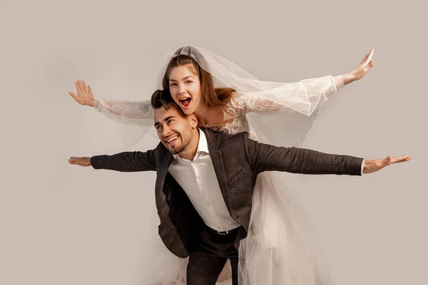 Cheerful bride piggybacking on happy groom isolated on grey — Fotografia de Stock