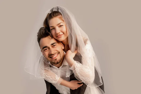 Lächelnde Braut huckepack auf glücklichem Bräutigam isoliert auf grau mit Fliederton — Stockfoto
