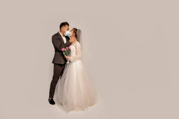 Bride and groom in medical masks kissing isolated on grey with lilac shade — Photo de stock