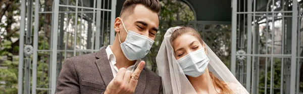 Junger Mann zeigt Ehering neben Braut in medizinischer Maske, Banner — Stockfoto
