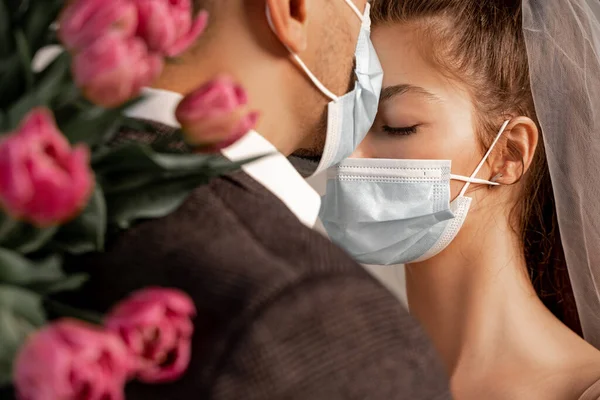 Young bride in medical mask near groom and tulips on blurred foreground — Photo de stock