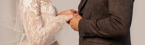 Partial view of bride and groom holding hands isolated on grey, banner - foto de stock