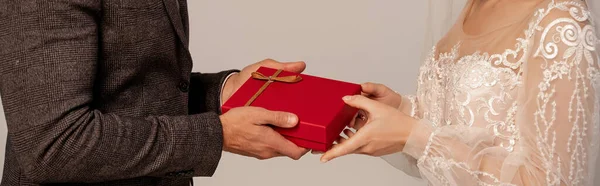 Partial view of groom presenting gift box to bride isolated on grey, banner — Photo de stock