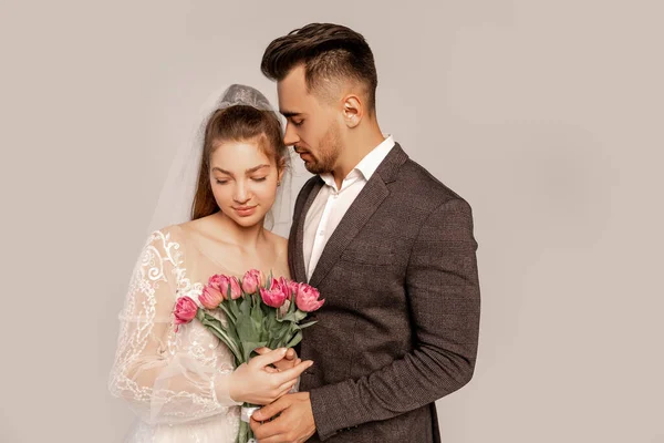 Junger Mann in der Nähe charmante Braut mit frischen Tulpen isoliert auf grau — Stockfoto