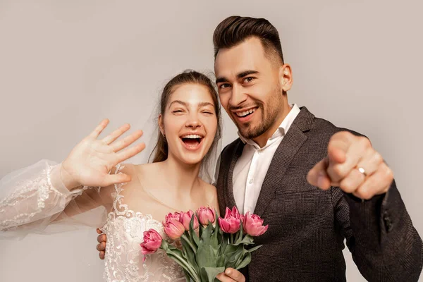 Cheerful couple pointing with finger and waving hand isolated on grey with lilac shade — Fotografia de Stock