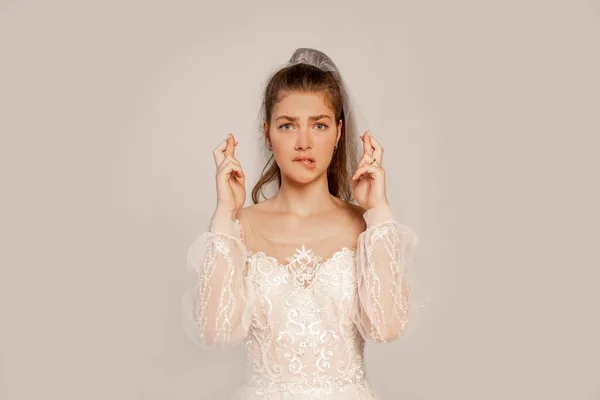 Worried woman in wedding dress with crossed fingers isolated on grey — Fotografia de Stock