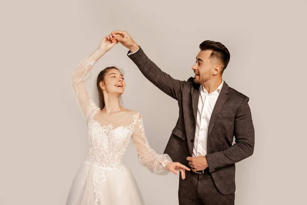 Glückliches junges Brautpaar tanzt isoliert auf grau mit fliederfarbenem Schatten — Stockfoto