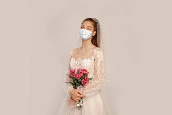 Young bride in safety mask holding fresh tulips isolated on grey with lilac shade — Stock Photo