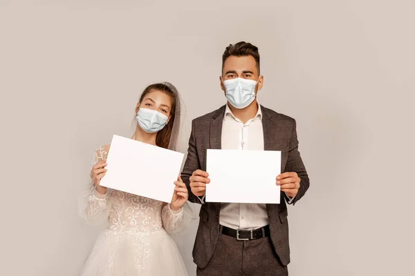 Young couple in medical masks holding blank placards isolated on grey — Stock Photo