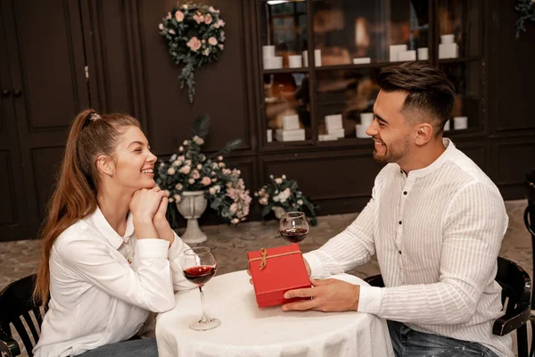Smiling man presenting gift to happy young woman in restaurant - foto de stock