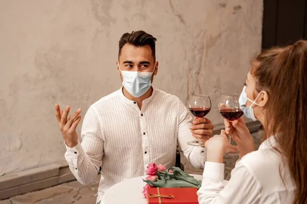 Young man in medical mask gesturing while toasting with wine glass near woman in cafe — Photo de stock
