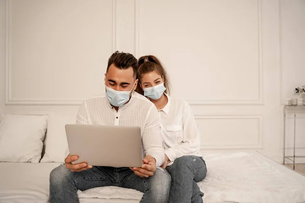 Couple in safety masks watching movie on laptop during quarantine at home - foto de stock