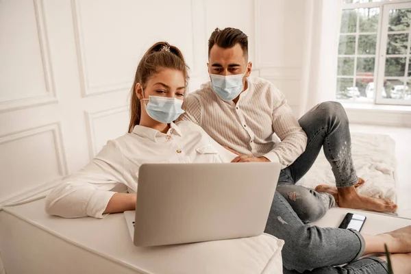 Young couple in medical masks watching movie on laptop at home — Fotografia de Stock