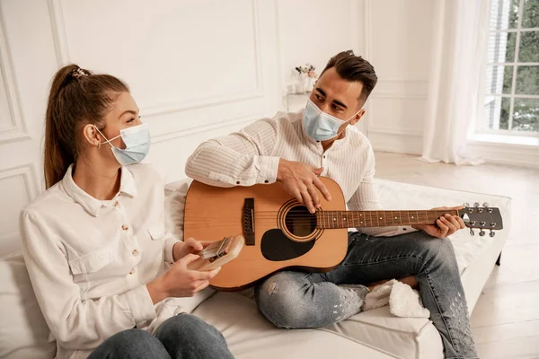 Пара в защитных масках играет на музыкальных инструментах в гостиной — стоковое фото