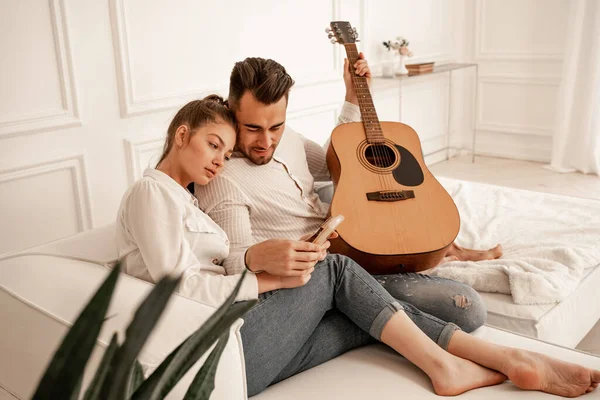 Молода пара сидить на дивані з акустичною гітарою і Каламбо — стокове фото