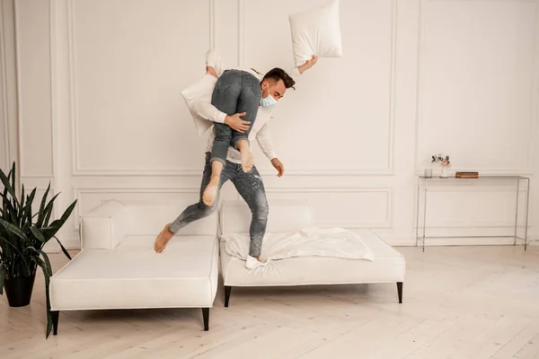 Young man in safety mask holding girlfriend while fooling around in living room - foto de stock