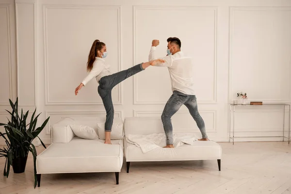 Junges Paar in Schutzmasken kämpft auf Couch, während es zu Hause herumalbert — Stockfoto