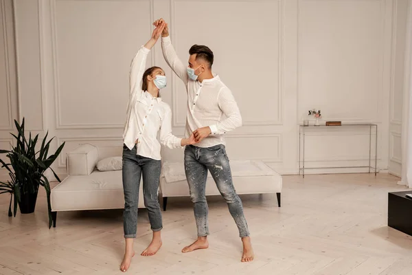 Young barefoot couple in jeans and medical masks dancing at home — Fotografia de Stock